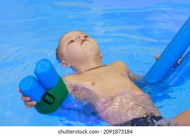 Rehabilitation Of A Child With Down Syndrome In A Pool, A Boy Swims In Blue Water.
