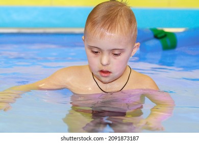 Rehabilitation Of A Child With Down Syndrome In A Pool, A Boy Swims In Blue Water.
