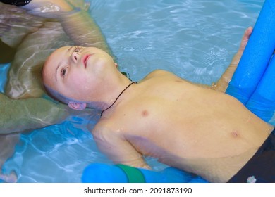 Rehabilitation Of A Child With Down Syndrome In A Pool, A Boy Swims In Blue Water.
