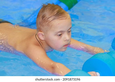 Rehabilitation Of A Child With Down Syndrome In A Pool, A Boy Swims In Blue Water.
