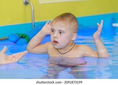 Rehabilitation Of A Child With Down Syndrome In A Pool, A Boy Swims In Blue Water.
