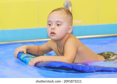 Rehabilitation Of A Child With Down Syndrome In A Pool, A Boy Swims In Blue Water.
