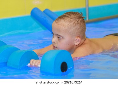 Rehabilitation Of A Child With Down Syndrome In A Pool, A Boy Swims In Blue Water.
