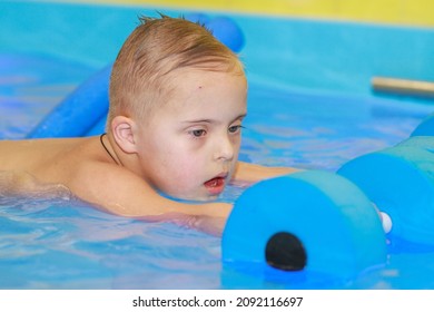 Rehabilitation Of A Child With Down Syndrome In A Pool, A Boy Swims In Blue Water.
