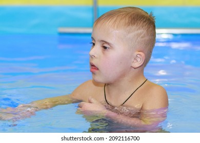 Rehabilitation Of A Child With Down Syndrome In A Pool, A Boy Swims In Blue Water.
