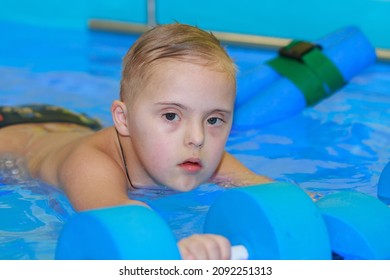 Rehabilitation Of A Child With Down Syndrome In A Pool, A Boy Swims In Blue Water.
