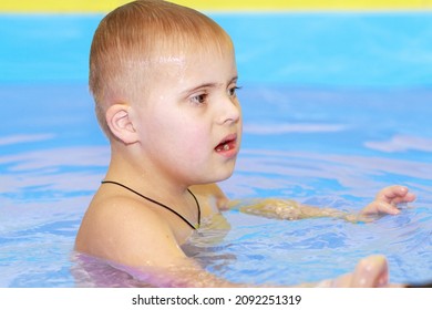 Rehabilitation Of A Child With Down Syndrome In A Pool, A Boy Swims In Blue Water.
