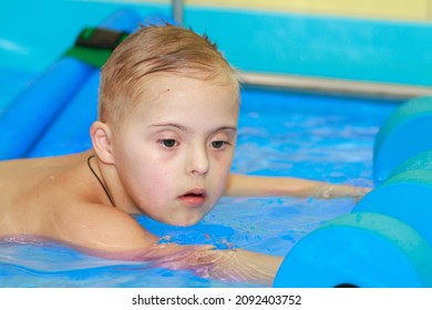 Rehabilitation Of A Child With Down Syndrome In A Pool, A Boy Swims In Blue Water.
