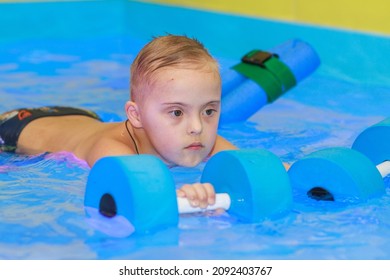 Rehabilitation Of A Child With Down Syndrome In A Pool, A Boy Swims In Blue Water.
