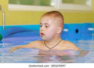 Rehabilitation Of A Child With Down Syndrome In A Pool, A Boy Swims In Blue Water.
