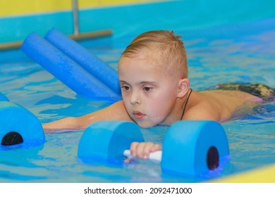 Rehabilitation Of A Child With Down Syndrome In A Pool, A Boy Swims In Blue Water.
