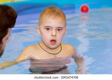 Rehabilitation Of A Child With Down Syndrome In A Pool, A Boy Swims In Blue Water.
