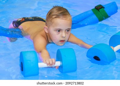 Rehabilitation Of A Child With Down Syndrome In A Pool, A Boy Swims In Blue Water.
