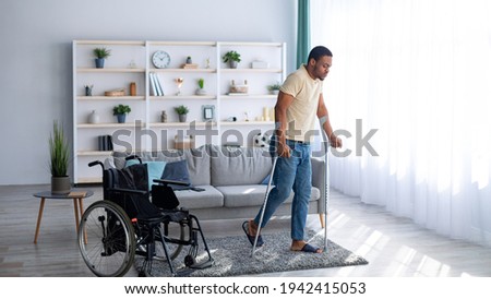 Rehabilitation concept. Young black guy walking with crutches after using wheelchair at home, panorama