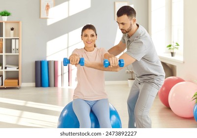 Rehabilitation exercise help with dumbbells, spinal therapy by male physical therapist in medical room. Woman patient, med coach, nurse training back, improving posture, body health, muscle-building - Powered by Shutterstock