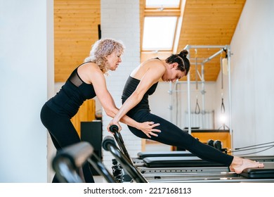 Rehabilitation, Healthy Lifestyle, Small Business Concept. Professional Mature Female Fitness Coach Teaching Girl Learn The Correctly Exercise On Pilates Reformer Bed.