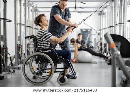 Rehabilitation specialist helps a guy in a wheelchair to do exercise on decompression simulator for recovery from injury