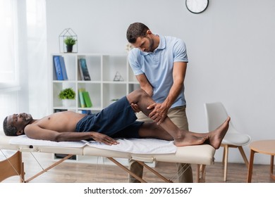 Rehabilitologist Treating Middle Aged African American Man Lying On Massage Table