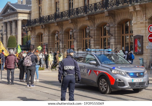 Reims, France - March 2021 - The brand-new\
Peugeot 5008 of the National Police, with blue flashing lights on,\
and a female police officer in intervention on Rue de Vesle during\
a demonstration