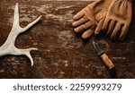 Reindeer antlers, leather gloves and a hunting knife on a rustic wooden table - top view