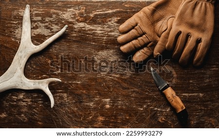 Reindeer antlers, leather gloves and a hunting knife on a rustic wooden table - top view