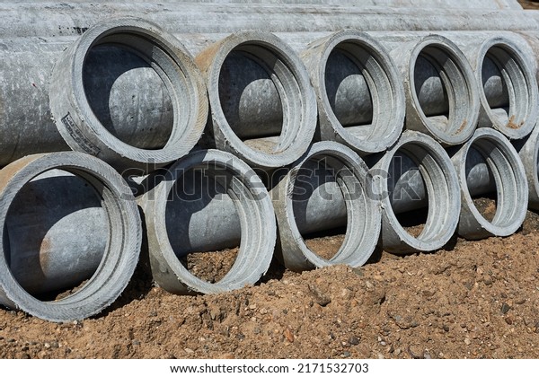 Reinforced concrete pipes and connecting\
rings lie on the sand. Sewer repair in the\
city.