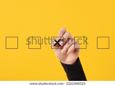 Rejection, cancellation, decline, wrong decision or choice concept. Male hand draws a cross x symbol in the middle of checkboxes on yellow background.