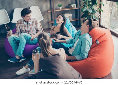 Rejoice And Cheerful Trandy Youths Sitting In A Loft Style Room With Coffee In Hands Tell Funny Stories And Humorous Joke To Each Other And Aloud Laugh Without Restraint With Big Toothy Smile