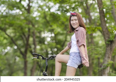 Rejoicing happy woman with mini bicycle in summer or spring forest. Asian female model.