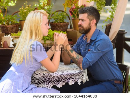 Relations and problems concept. Man with serious face and sad girlfriend. Couple have important conversation and holding hands. Couple in love sit in cafe outdoor, urban background.