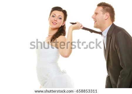 Relationship command concept. Dominant bride wearing wedding dress pulling groom tie, isolated.