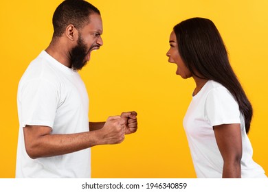 Relationship Crisis Concept. Side view profile portrait of African American couple arguing, angry displeased black woman and man yelling at each other and gesturing, yellow studio background