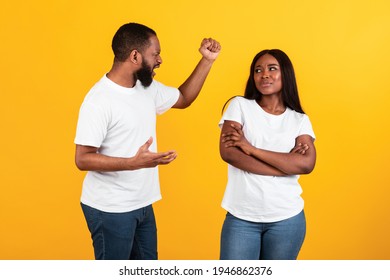 Relationship Problem. Portrait of African American couple arguing, angry displeased black man screaming at his wife who ignoring him, husband raising hand with clenched fist, yellow studio background