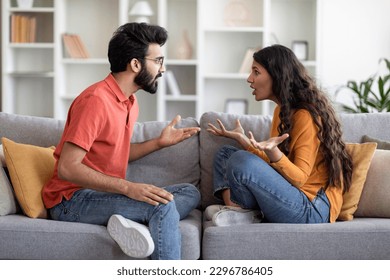 Relationship Problems. Portrait Of Young Indian Couple Arguing At Home, Eastern Millennial Spouses Sitting On Couch And Screaming At Each Other, Suffering Misunderstanding And Marriage Crisis - Shutterstock ID 2296786405