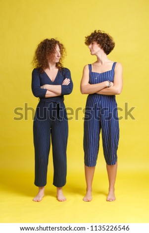 Relationship problems. Two young charming girls keeps hands crossed, offended at each other. A grim red-haired woman is holding offense at her older sister. Rancor and forgiveness