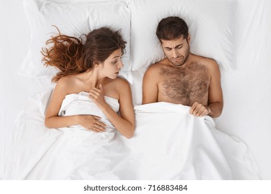 Relationships difficulties, stress and impotence. Couple having marital problems. Woman and man in bed looking under blanket, feeling unhappy and frustrated while husband having erectile dysfuntion