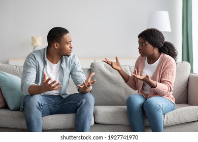 Relationships problems and crisis concept. Angry black man and woman sitting on couch at home, having quarrel, copy space. Furious african american guy and lady yelling at each other