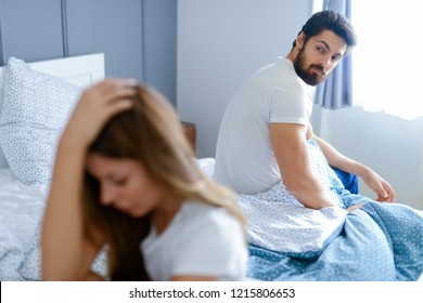 Relationships Problems. Young Couple Sitting In A Bedroom And Fighting. Both Of Them Looking Sad And Disappointed.