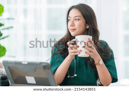 relax after work ,asian female doctor hand hold hot coffee drink cup casual relax after working hard telemedicine in clinic while wear uniform 