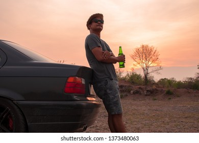 Relax Asian Man Holding Beer Inside Car Trunk With Sunset.