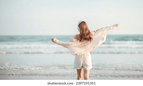 Relax asian woman wearing headphones walking in the sea beach at golden sunset - Female tourist listening to music on summer vacation - Powered by Shutterstock