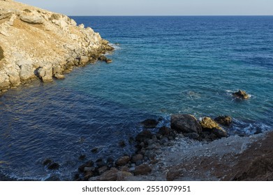 Relax by the calm sea as waves gently lap against the rocky shoreline under a fading sunset. - Powered by Shutterstock