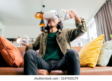 relax casual Asian adult Man Wearing Virtual Reality Headset and Holding Controllers Plays in a sport Video Game at Home. Playing VR active sport game online in the Living Room - Powered by Shutterstock