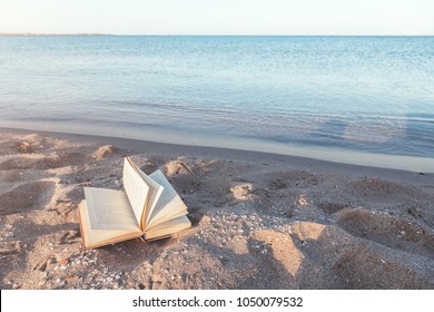 Relax concept. Open book on sand near the sea. Summer vacations still life. The text is transformed and not recognizable. - Powered by Shutterstock