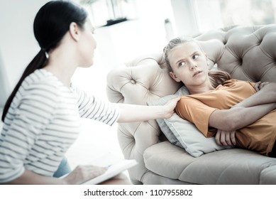 Relax Darling. Grumpy Teen Girl Lying On Sofa While Looking At Kind Female Psychologist Who Sitting With Notebook