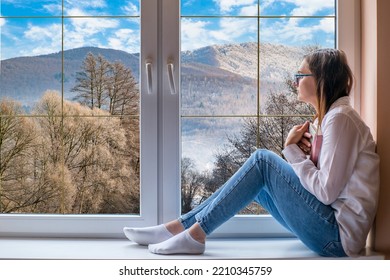 Relax At Home. The Girl Sits On The Windowsill And Looks At The Mountains. Hobby Time