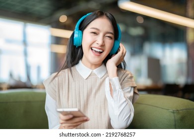 Relax Joyful Casual Asian Female Adult Woman Casual Cloth Enjoy Listening Music From Streaming Online Playing Music Playlist Application On Smartphone Via Earphone  On Sofa Couch At Co Working Space  