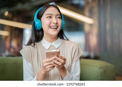 Relax Joyful Casual Asian Female Adult Woman Casual Cloth Enjoy Listening Music From Streaming Online Playing Music Playlist Application On Smartphone Via Earphone  On Sofa Couch At Co Working Space  