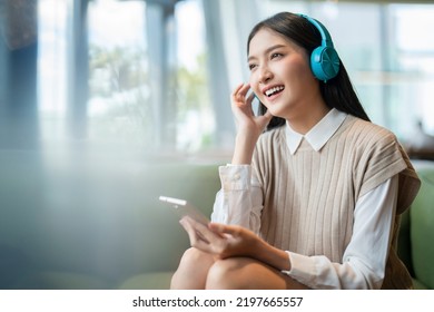 Relax Joyful Casual Asian Female Adult Woman Casual Cloth Enjoy Listening Music From Streaming Online Playing Music Playlist Application On Smartphone Via Earphone On Sofa Couch At Co Working Space  