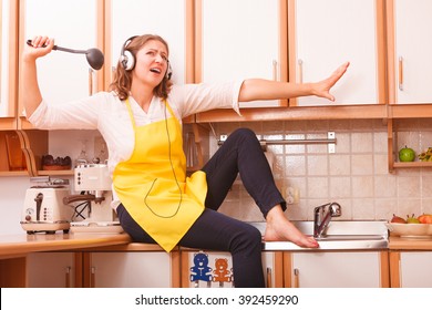 Relax In Kitchen. Listening Music Singing And Dancing. Funny Happy Housewife Cook Chef With Earphones Wearing Yellow Apron Sitting And Relaxing At Home.